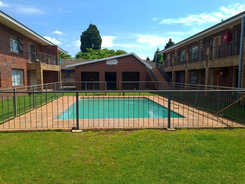 Communal swimming pool area featuring a paved surround, metal safety fencing, and surrounding brick apartment buildings with lawn space.