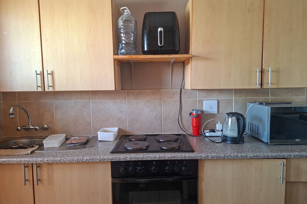 A functional kitchen featuring light wood-finish cabinetry, a tiled splashback, integrated electric hob, and built-in oven with ample counter space.