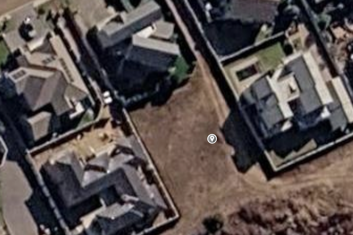 An aerial view of a vacant residential land plot situated between existing developed properties in a suburban neighborhood.