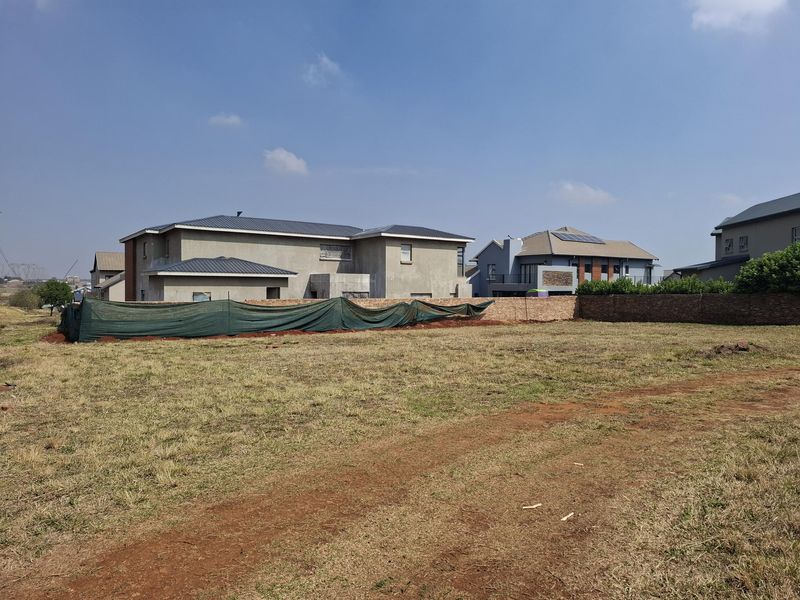 A vacant residential plot of land featuring a brick boundary wall and temporary shade cloth fencing, situated in a developed suburban estate.