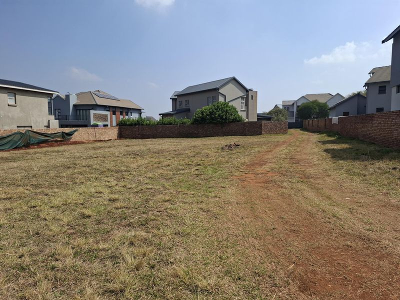 A vacant residential plot featuring a level grass surface and established brick boundary walls, situated within a developed residential estate.