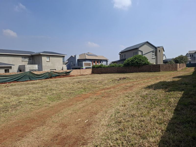 A vacant residential plot featuring a brick boundary wall, situated in a developed neighborhood with surrounding modern homes.