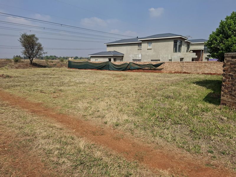 A vacant residential plot featuring a brick boundary wall with shade netting, offering a clear space for future development.