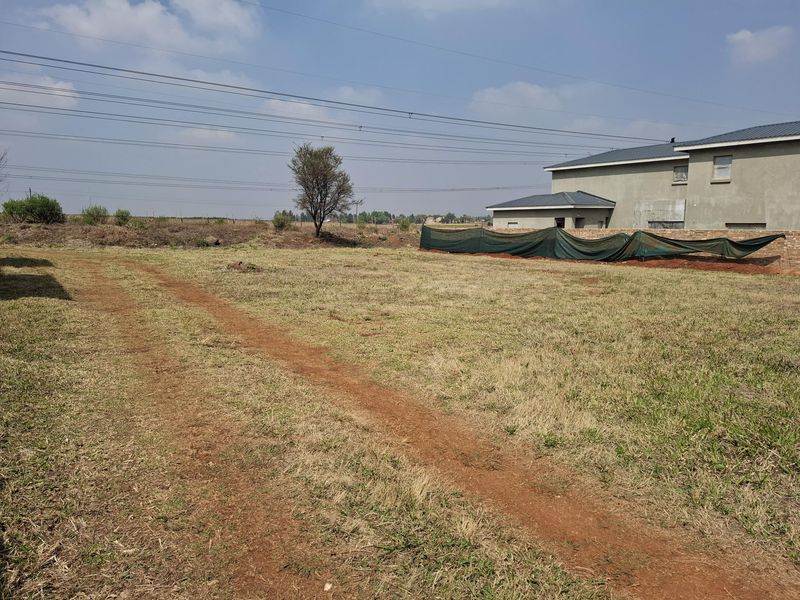 A view of a vacant residential plot featuring a dirt track, natural grass, and adjacent property boundary fencing.