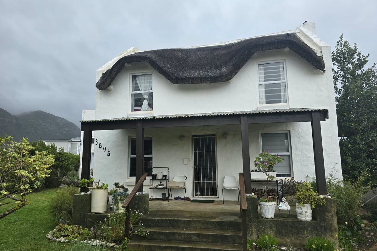Charming double-story cottage featuring a traditional thatched roof, a covered front porch, and a secure entrance, set within a landscaped garden.