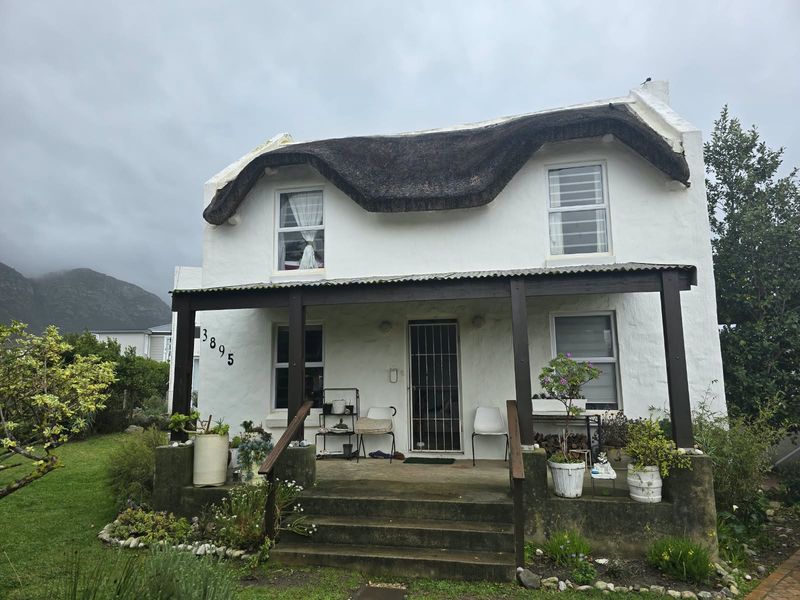 Charming double-story cottage featuring a traditional thatched roof, a covered front porch, and a secure entrance, set within a landscaped garden.