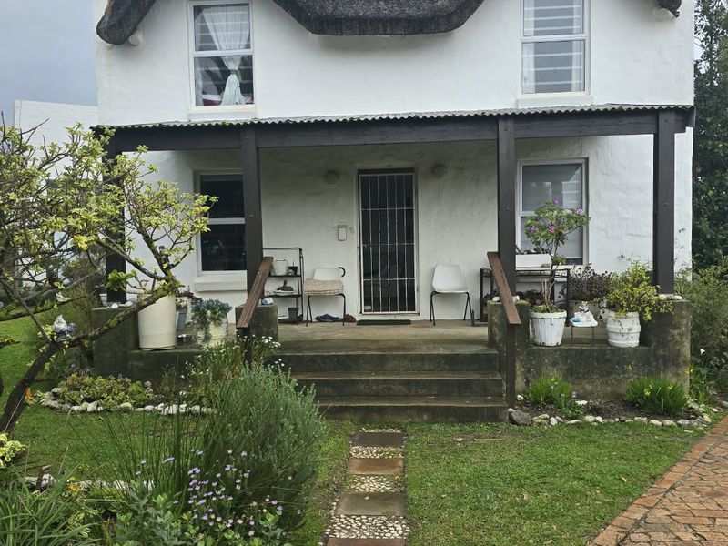 A charming cottage-style home featuring a traditional thatched roof, a covered front porch, and a brick-paved walkway set within a garden.