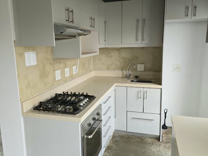 A functional kitchen featuring light-toned cabinetry, stone countertops, a gas hob, and an integrated oven, set against an exposed timber ceiling.