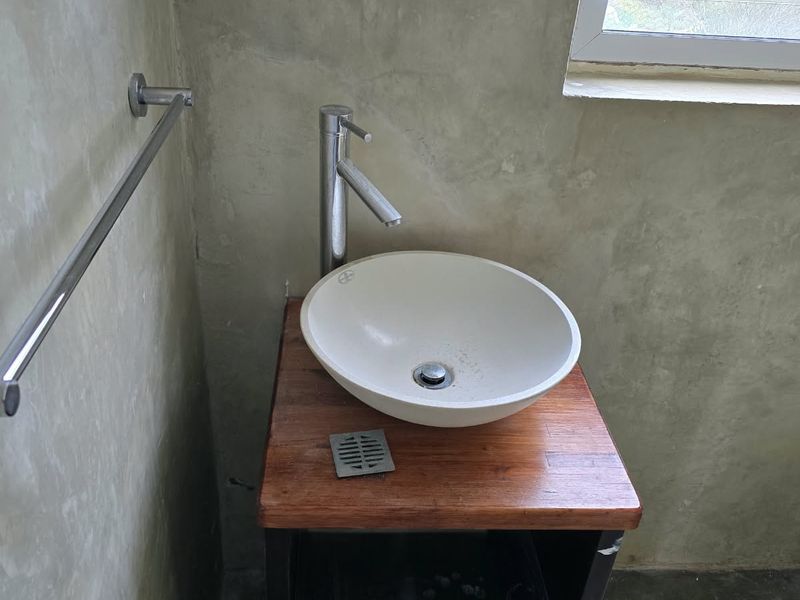 A compact bathroom vanity featuring a vessel sink on a timber top, set against a raw concrete wall finish with a functional louvre window.
