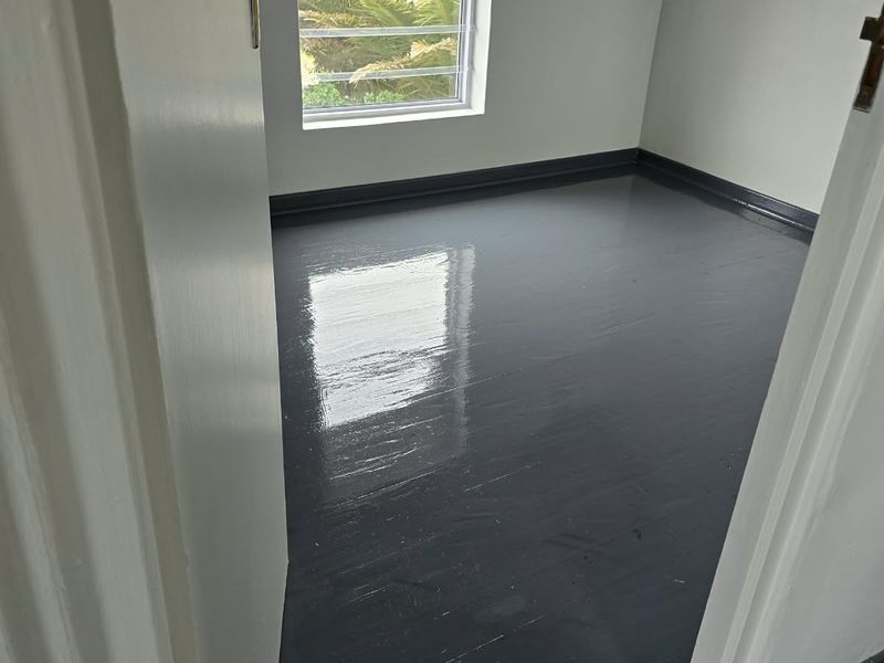 An empty bedroom featuring painted dark grey timber flooring, white walls, and an exposed timber roof beam.