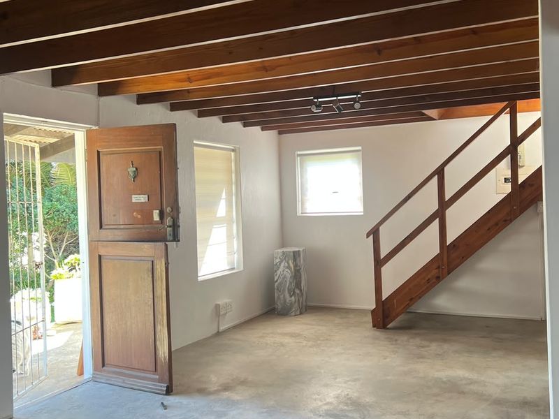 Open-plan living area featuring exposed timber ceiling beams, a wooden staircase, and a stable-style entrance door leading to the exterior.