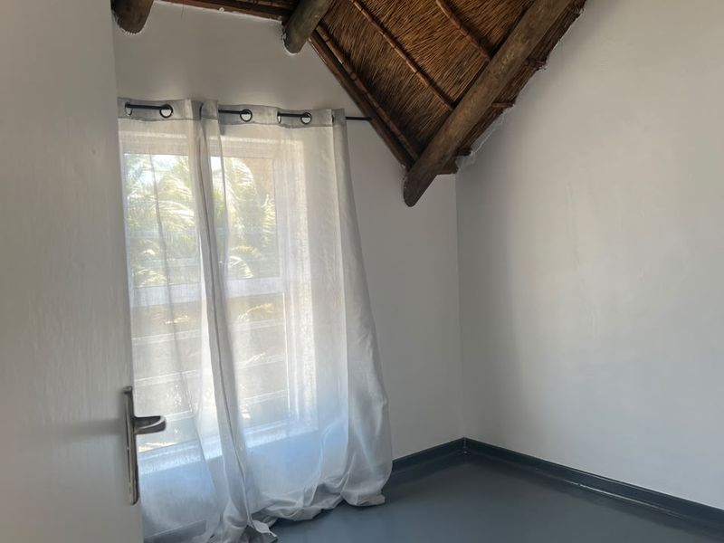 A bright, empty bedroom featuring a unique thatched roof with exposed timber rafters and painted flooring, offering a rustic yet clean aesthetic.