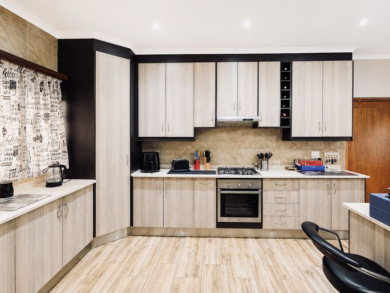 Modern kitchen featuring light wood-grain cabinetry, contrasting dark accents, built-in gas hob, oven, extractor fan, and tiled backsplash with durable laminate flooring.