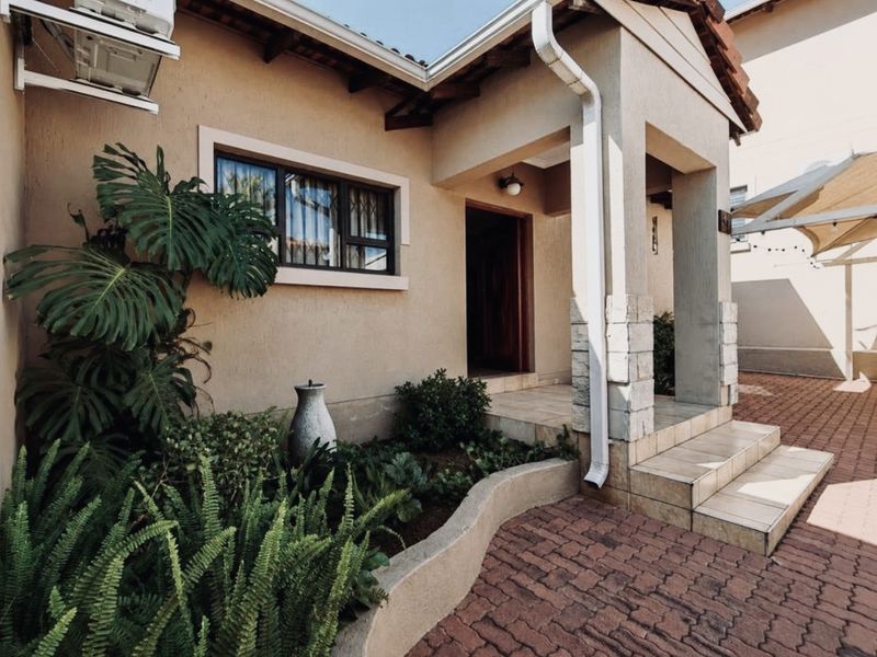A well-maintained front entrance featuring tiled steps, stone-clad pillars, and a brick-paved driveway with established garden landscaping.