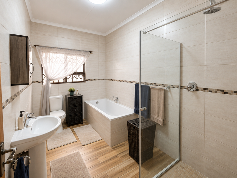 A well-maintained bathroom featuring a pedestal basin, a built-in bathtub, and a separate glass-enclosed shower with neutral wall tiling and wood-look flooring.