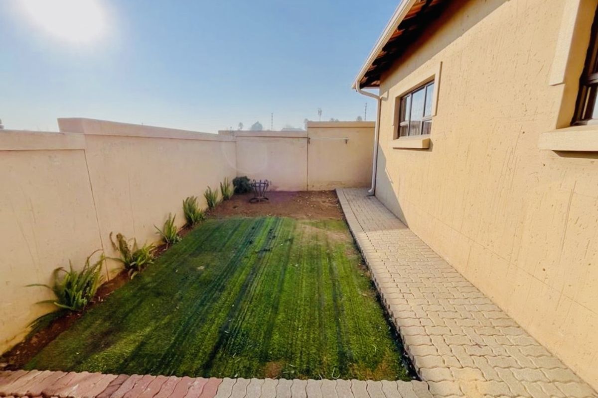 A private rear garden area featuring a paved walkway, perimeter walling, and a small section of artificial turf.