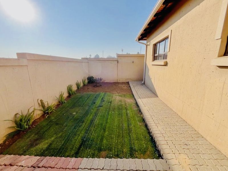 A private rear garden area featuring a paved walkway, perimeter walling, and a small section of artificial turf.