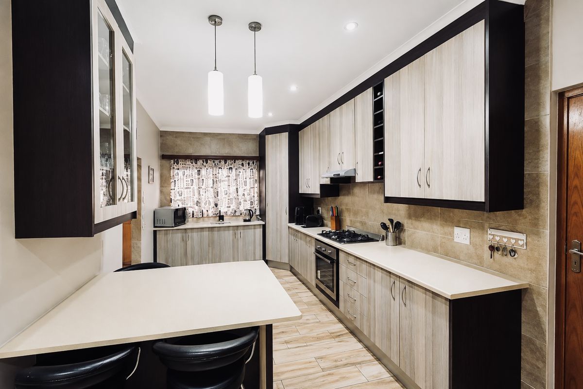 Modern kitchen featuring two-tone cabinetry, gas hob, built-in oven, extractor fan, tiled backsplash, and a breakfast nook area with pendant lighting.