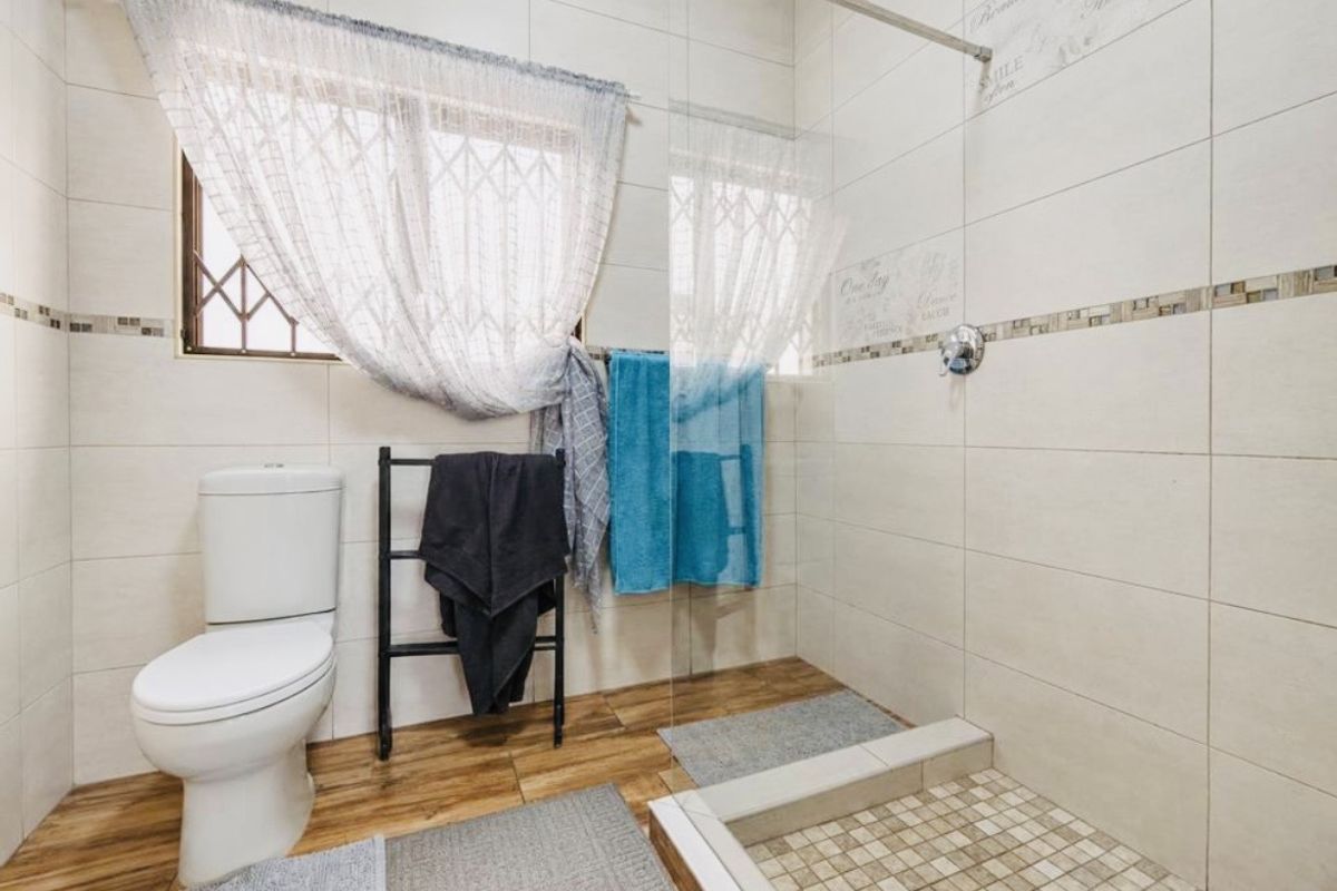 A modern bathroom featuring a walk-in shower with a glass screen, neutral wall tiling, and wood-look floor tiles.