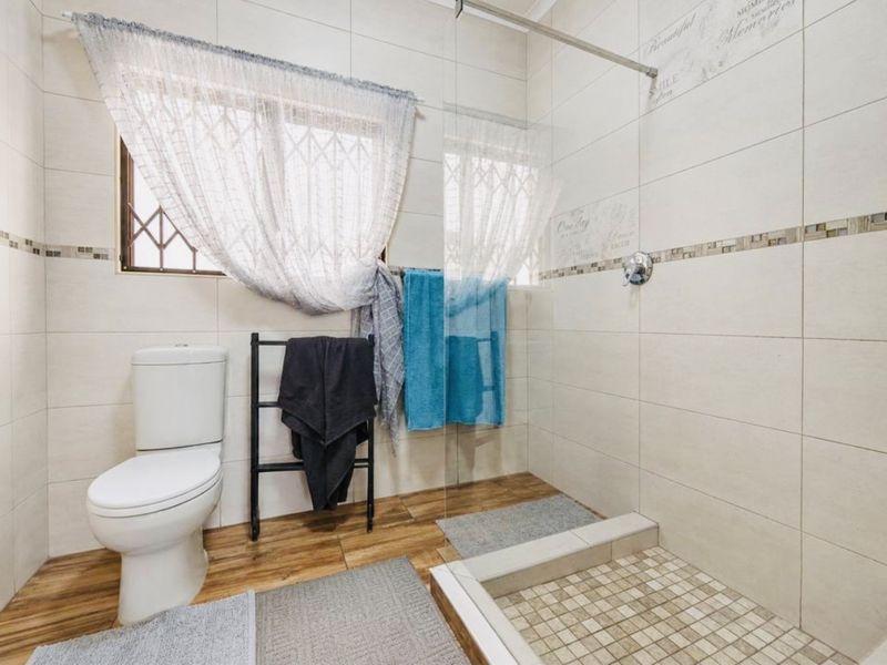 A modern bathroom featuring a walk-in shower with a glass screen, neutral wall tiling, and wood-look floor tiles.