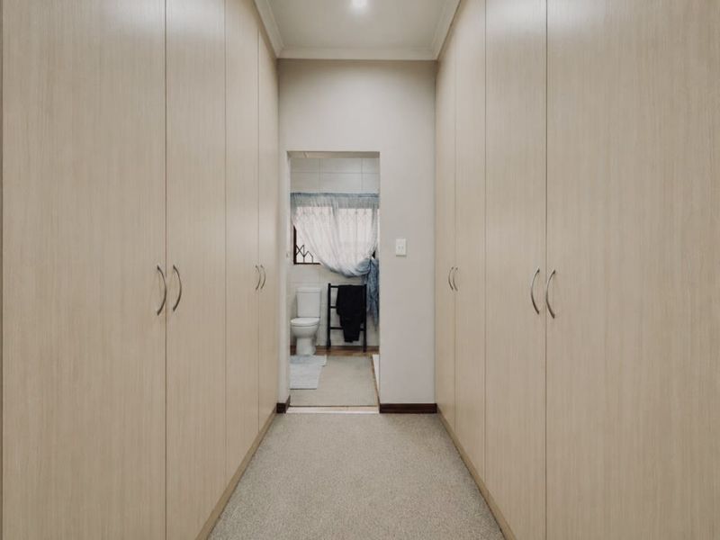 A clean hallway featuring extensive built-in cupboards providing ample storage space, leading directly into an adjoining bathroom.