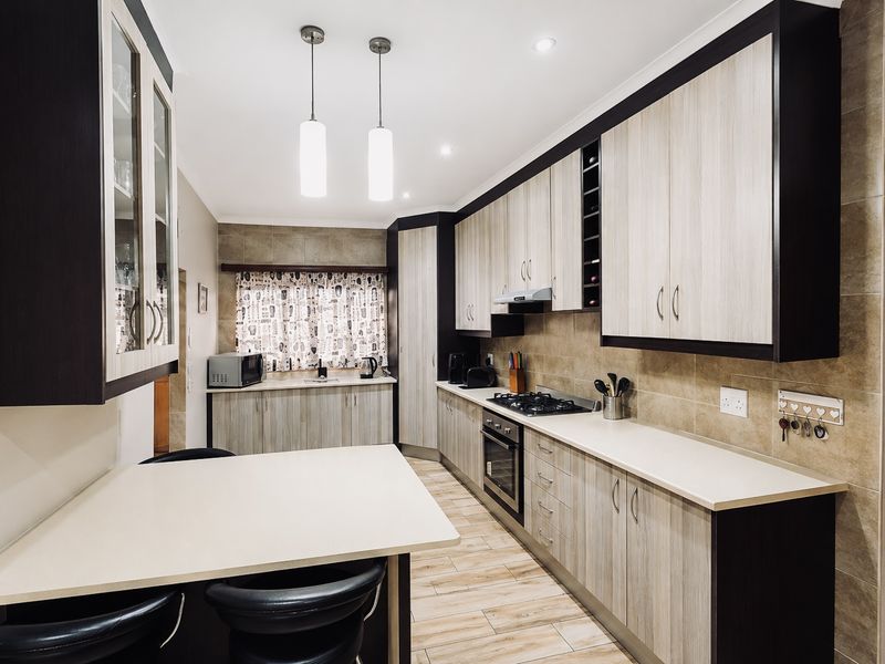 Modern kitchen featuring two-tone cabinetry, gas hob, built-in oven, extractor fan, tiled backsplash, and a breakfast nook area with pendant lighting.
