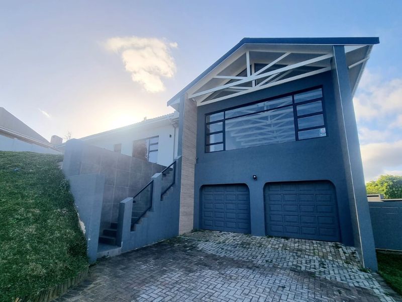 Modern double-story home exterior featuring a double garage, paved driveway, and an external staircase with glass balustrades leading to the upper level.
