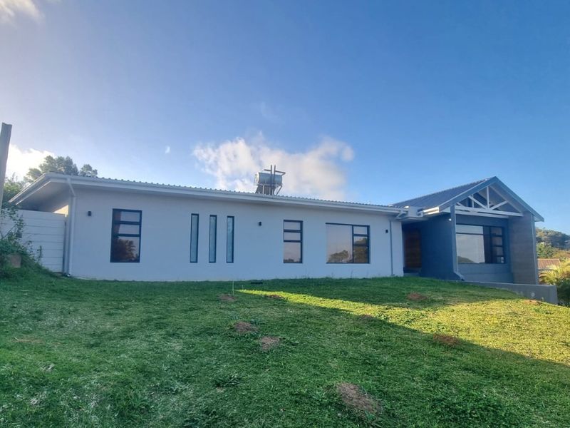 A well-maintained rear exterior view of a modern single-story house featuring a pitched roof, solar water heater, and large aluminium-framed windows.