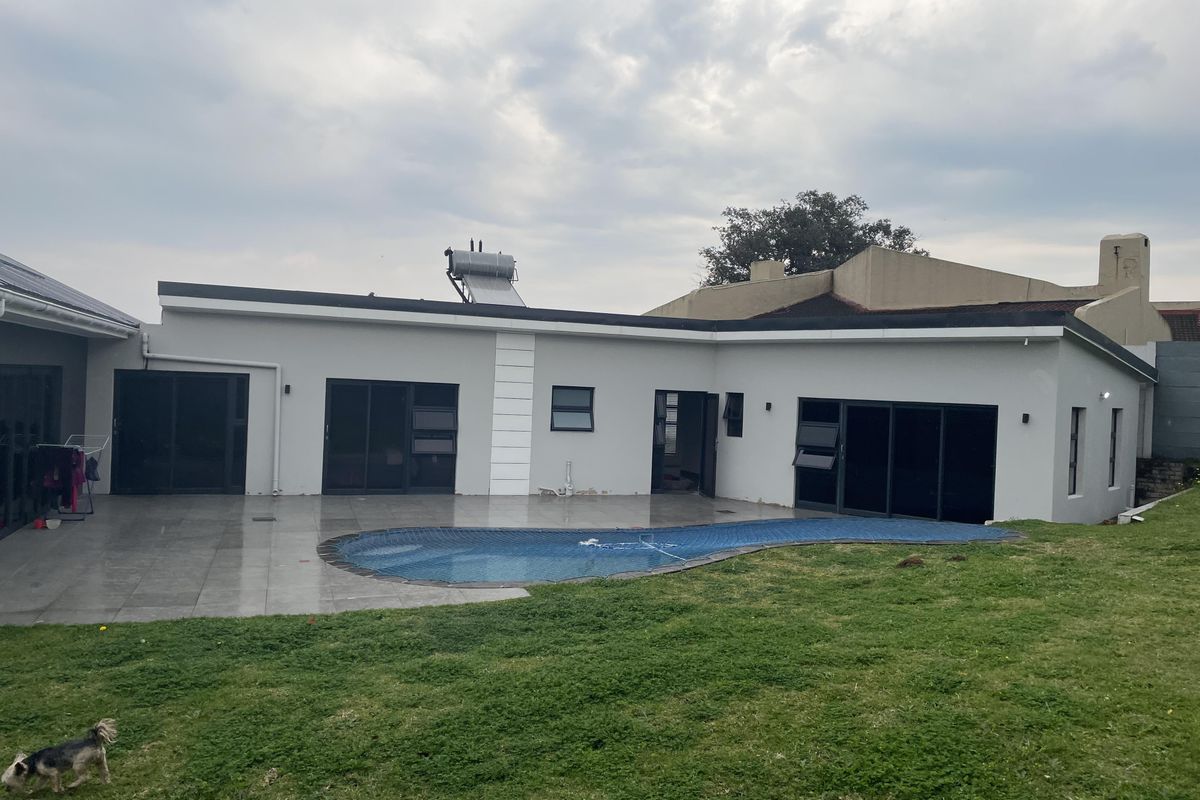 Rear view of the property featuring a tiled patio, swimming pool, and a well-maintained lawn with solar water heating infrastructure on the roof.
