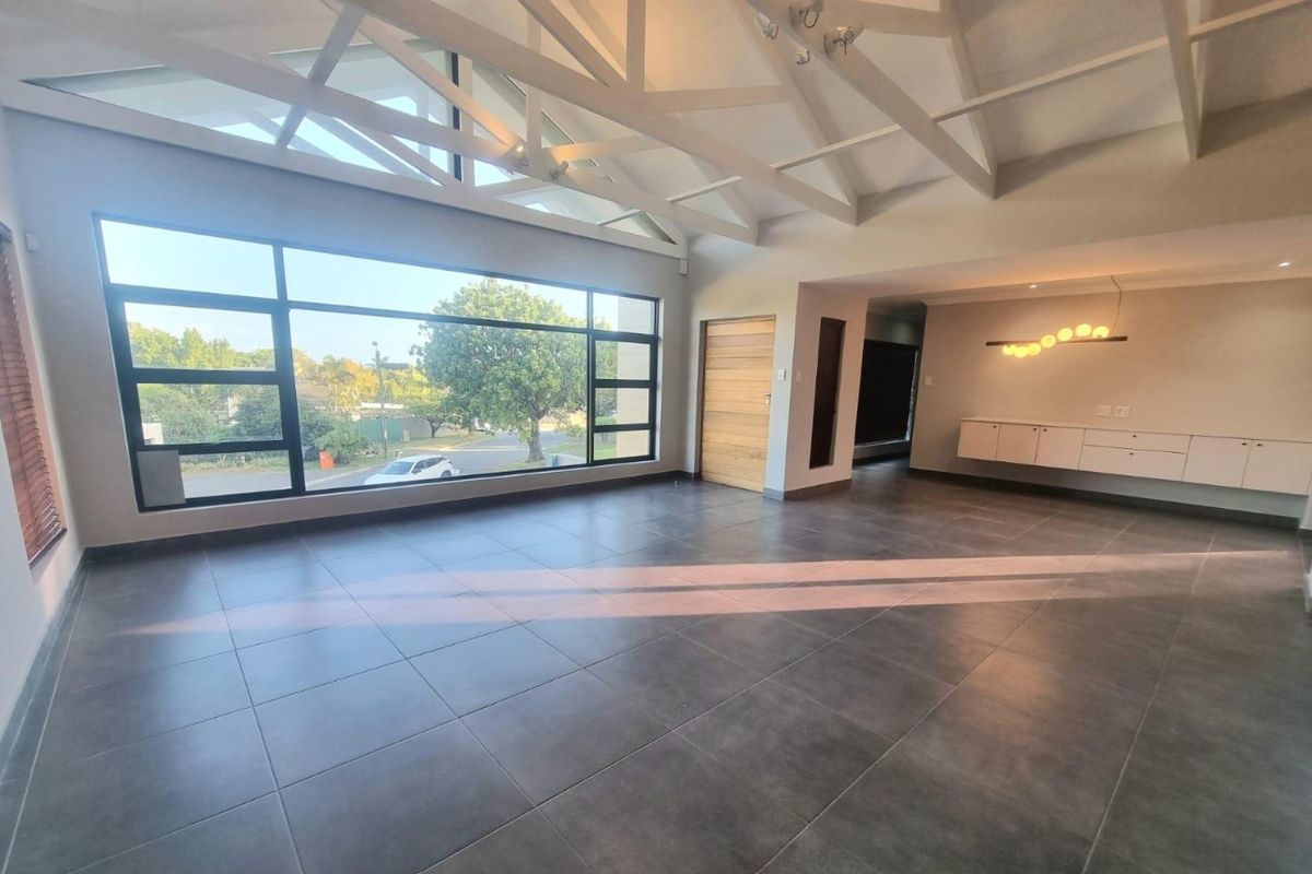 Spacious living area featuring high vaulted ceilings with exposed beams, large windows providing natural light, tiled floors, and sleek built-in wall cabinetry.
