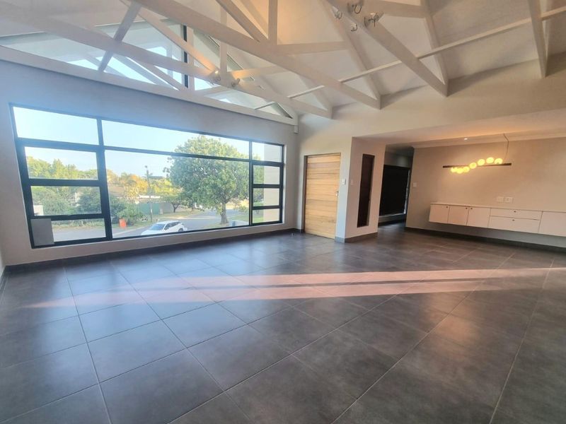 Spacious living area featuring high vaulted ceilings with exposed beams, large windows providing natural light, tiled floors, and sleek built-in wall cabinetry.