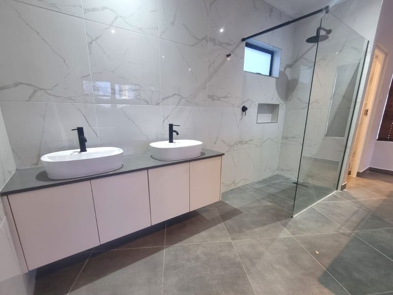 Modern bathroom featuring a floating double vanity with vessel sinks, matte black fixtures, and a spacious walk-in shower with marble-look wall tiling.