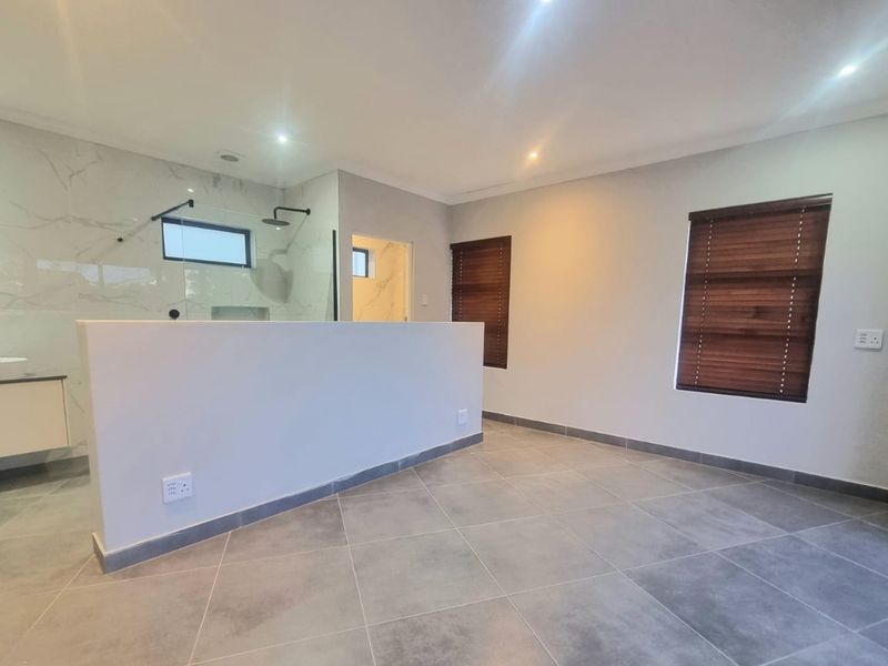 Modern bedroom featuring an open-plan en-suite bathroom with a walk-in shower, contemporary vanity, and neutral porcelain tiling throughout.