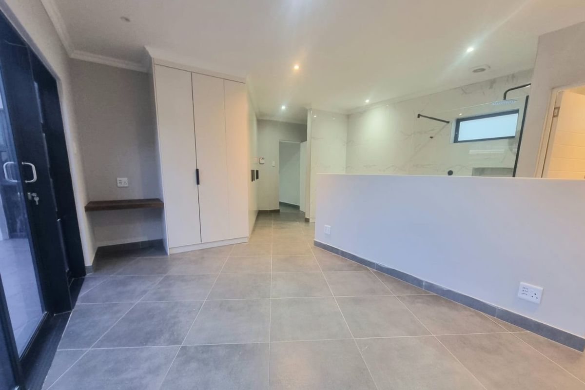Modern bedroom featuring large format floor tiles, built-in cabinetry, and an open-plan en-suite bathroom with a contemporary walk-in shower.