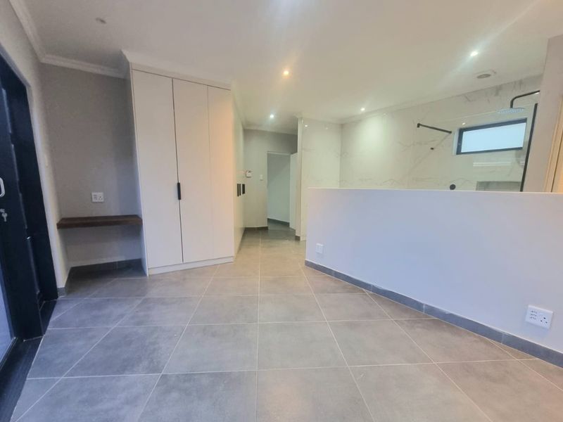 Modern bedroom featuring large format floor tiles, built-in cabinetry, and an open-plan en-suite bathroom with a contemporary walk-in shower.
