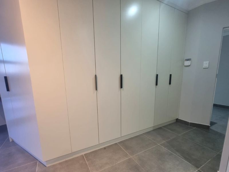 A clean, modern bedroom space featuring extensive built-in cupboards and neutral tiled flooring, offering a blank canvas for personalization.