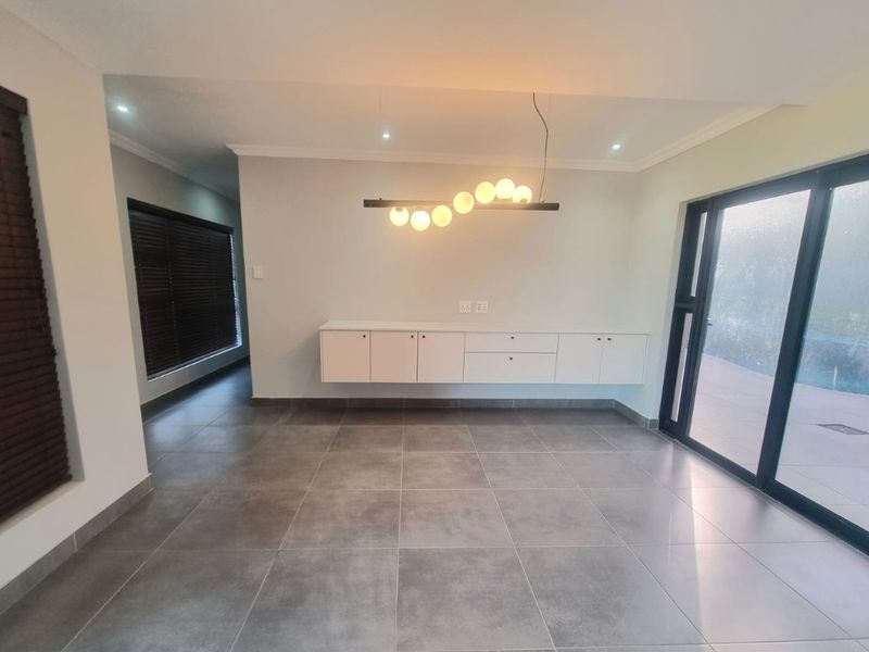 A bright, modern living area featuring large format floor tiles, custom floating cabinetry, and sliding glass doors leading to the outdoor space.
