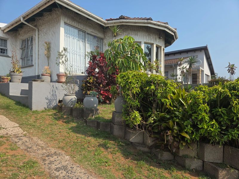 Front elevation of a house featuring a curved architectural design, security gates, and a concrete retaining wall with established garden landscaping.