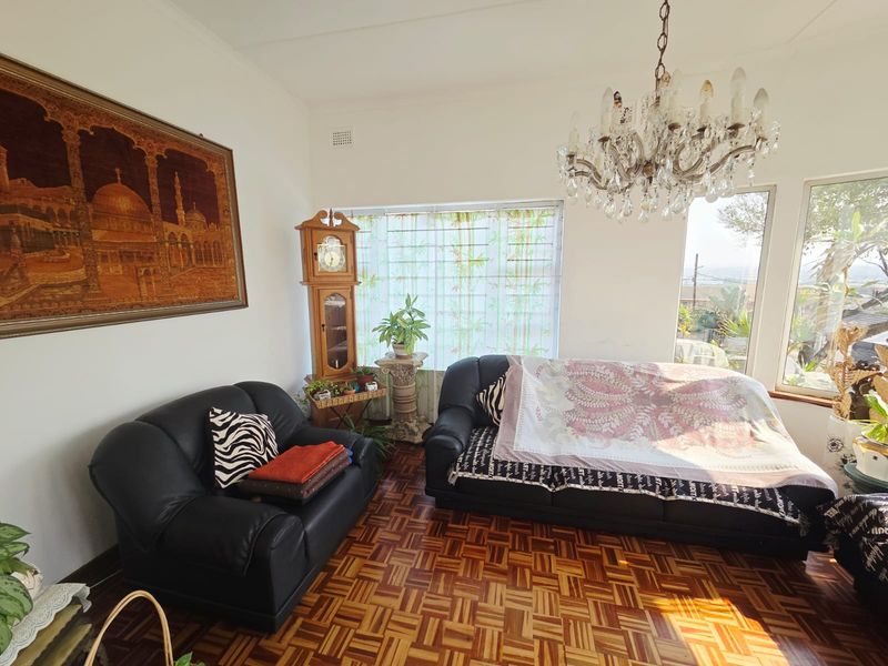 A living room featuring classic parquet flooring, a decorative crystal chandelier, and large windows that provide natural light and views.