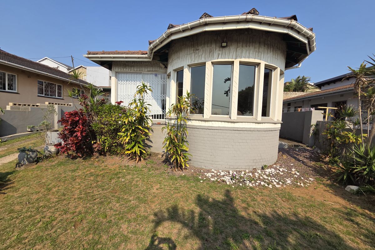 Rear view of the property featuring a distinctive curved bay window, tiled roof, and established garden area.