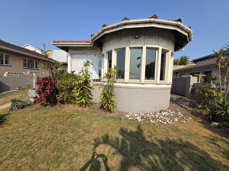 Rear view of the property featuring a distinctive curved bay window, tiled roof, and established garden area.