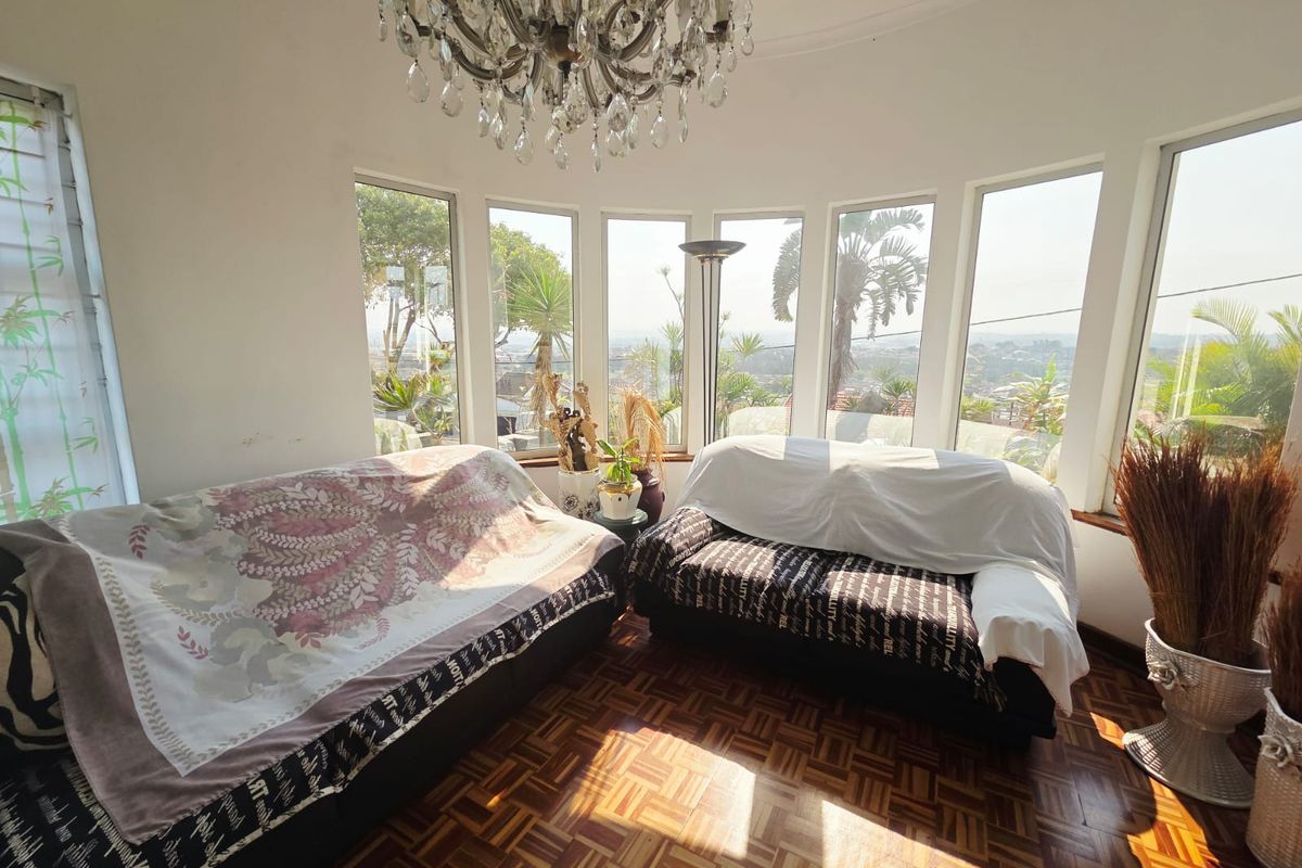 A bright living room featuring classic parquet flooring, a decorative crystal chandelier, and expansive bay windows offering panoramic views.