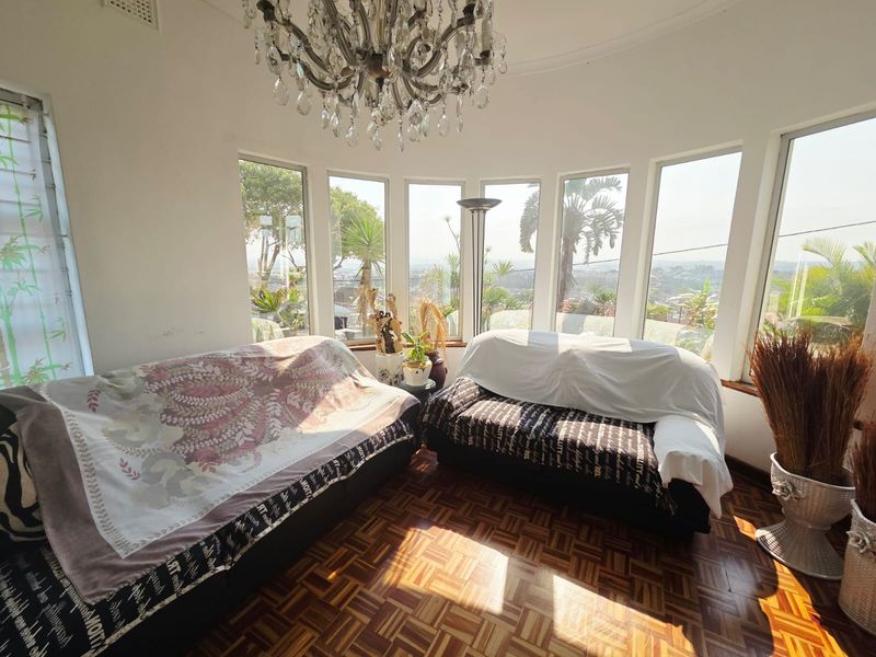 A bright living room featuring classic parquet flooring, a decorative crystal chandelier, and expansive bay windows offering panoramic views.