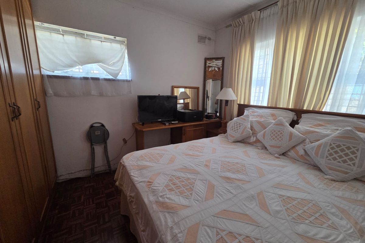 A functional bedroom featuring built-in wooden cupboards, parquet flooring, and large windows with curtain rails, offering a classic layout ready for modernization.