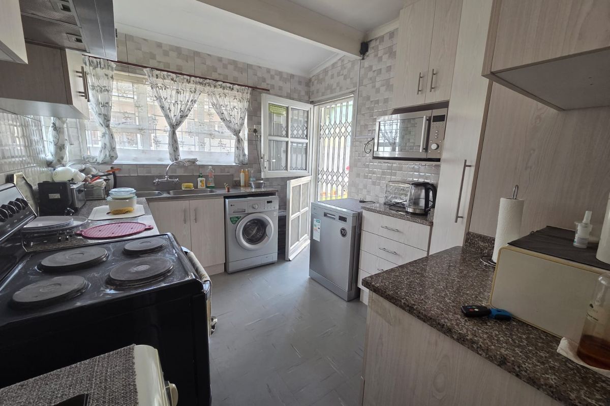 Functional kitchen featuring built-in cabinetry, laminate countertops, tiled backsplash, and integrated appliances with direct access to the exterior via a security gate.