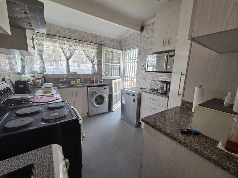 Functional kitchen featuring built-in cabinetry, laminate countertops, tiled backsplash, and integrated appliances with direct access to the exterior via a security gate.
