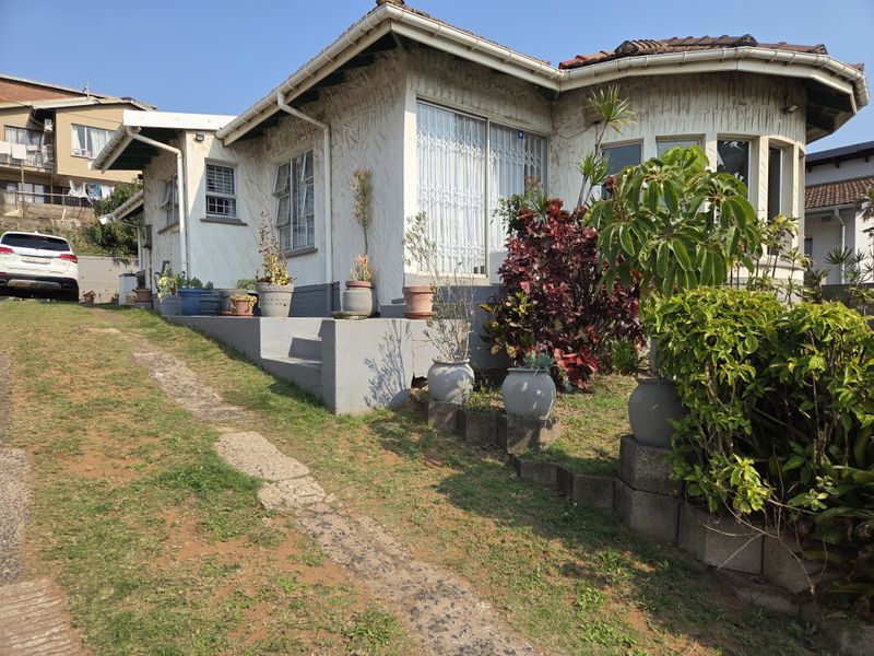 Front elevation of a single-story house featuring a tiled roof, security gates, and a concrete entrance area with a landscaped garden.