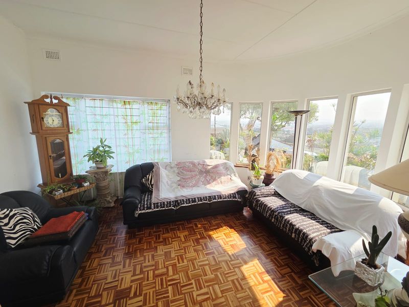 A bright living room featuring classic parquet flooring, a decorative crystal chandelier, and large windows offering natural light and views.