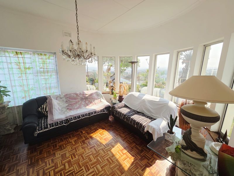 A bright living room featuring classic parquet flooring, a decorative crystal chandelier, and expansive bay windows offering natural light and scenic views.