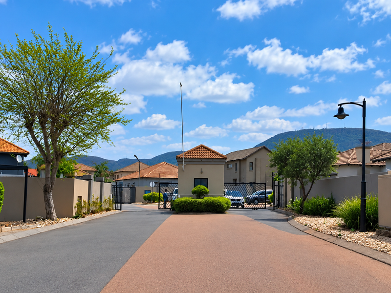 View of the secure gated entrance to the residential estate, featuring a guard house, paved driveway, and well-maintained perimeter walls.